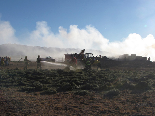 Firefighters put out burning hay bales in Iron County Sunday brought outside febced storage area by a tractor. Mark Havnes/The Salt lake Tribune